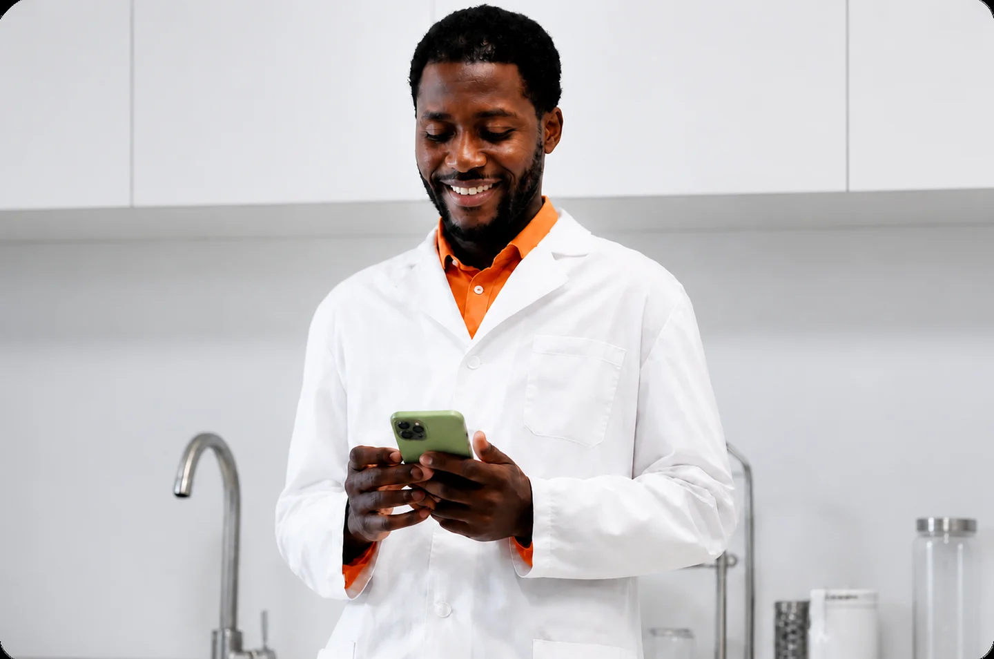 Homem de jaleco branco sorrindo enquanto olha o celular no laboratório