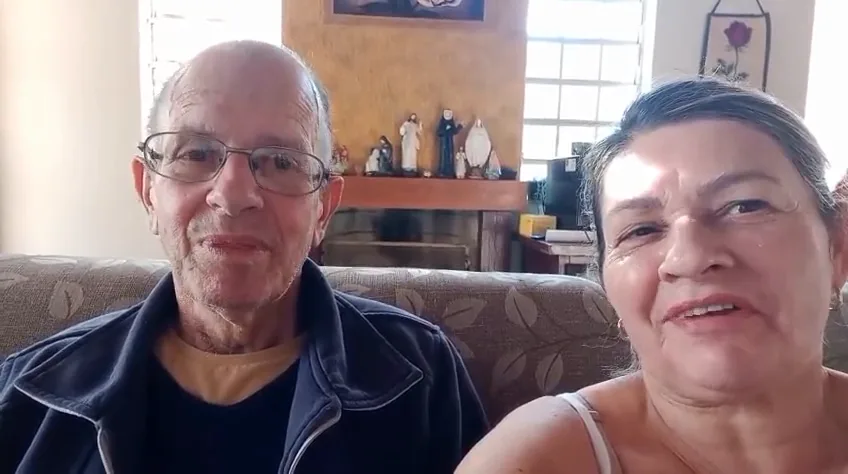 Antonio Roberto e Ana Lucia sentados no sofá de casa, gravando o depoimento