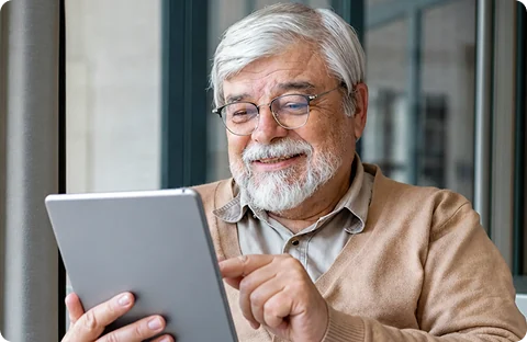 Senhor de cabelos brancos e óculos sorrindo enquanto usa um tablet